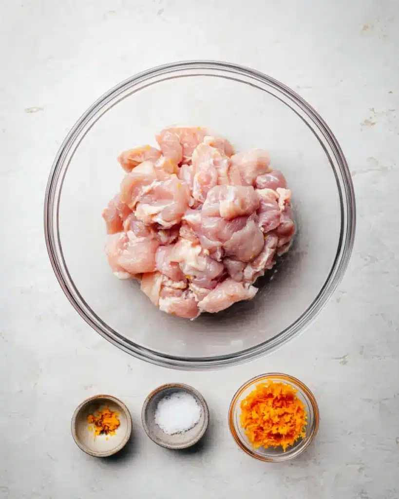 Raw chicken with orange zest and salt in glass bowls for orange chicken recipe