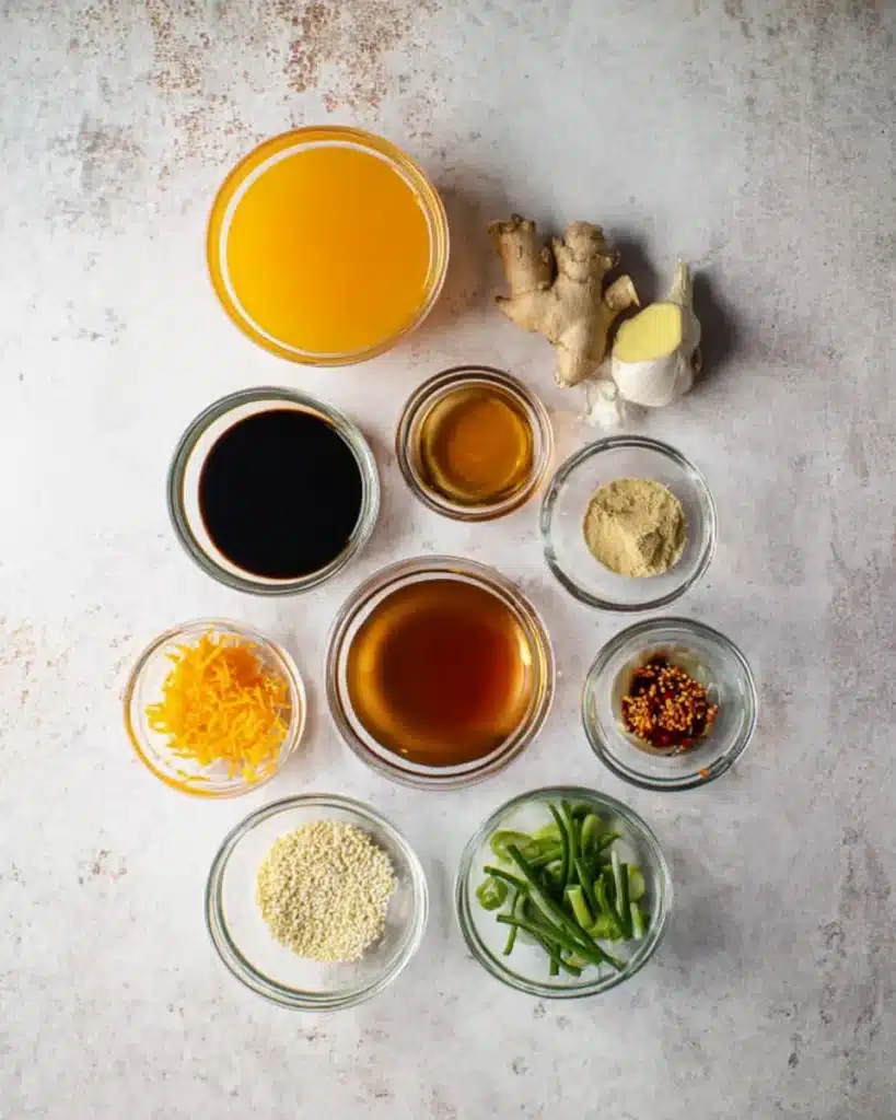 Orange chicken sauce ingredients in glass bowls on a marble surface
