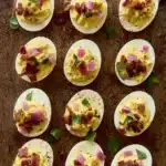 Thanksgiving deviled eggs topped with bacon, herbs, and onions on a rustic wooden surface