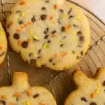 Pumpkin-shaped shortbread cookies with chocolate chips and colorful Halloween sprinkles on cooling rack