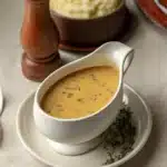 Golden vegan gravy in a white gravy boat with herbs