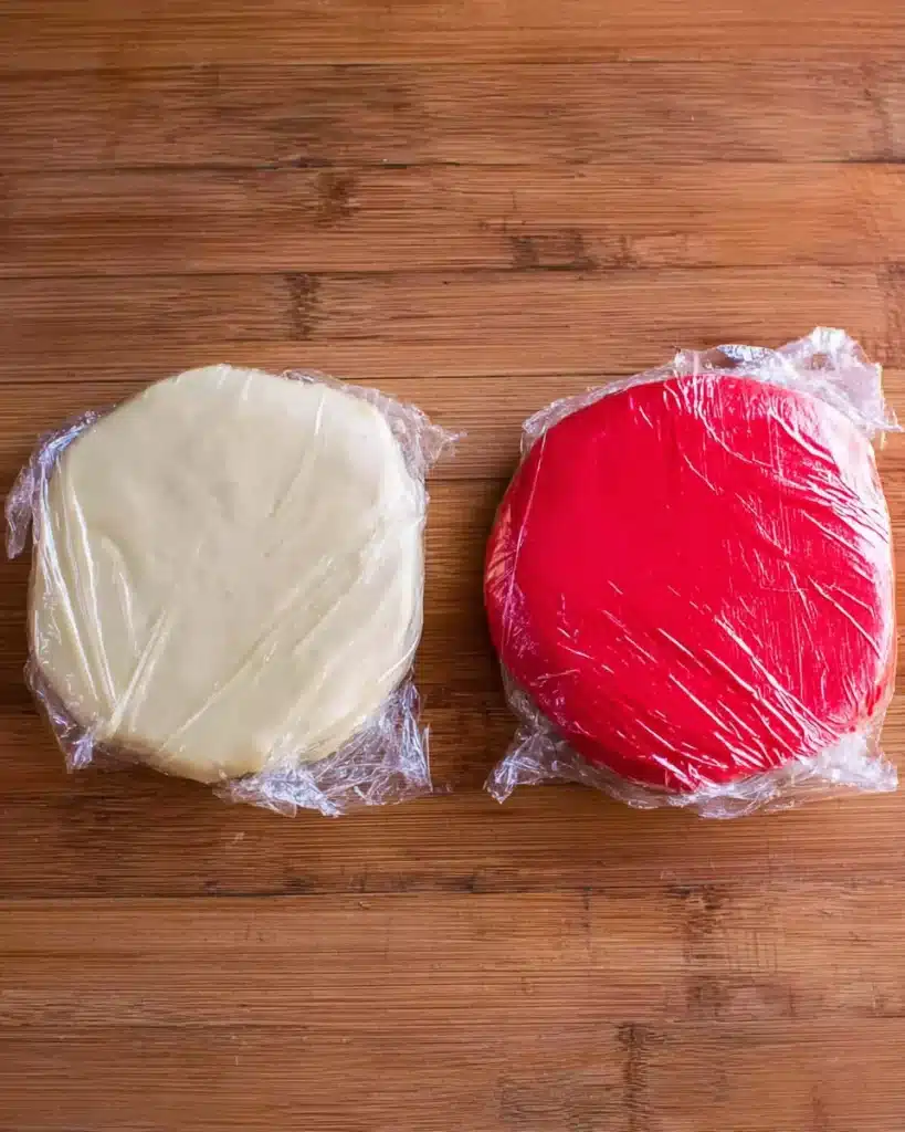 Red and white cookie dough disks wrapped in plastic on wooden surface