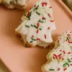 Christmas tree–shaped cake with white icing and red and green sprinkles on a pink plate