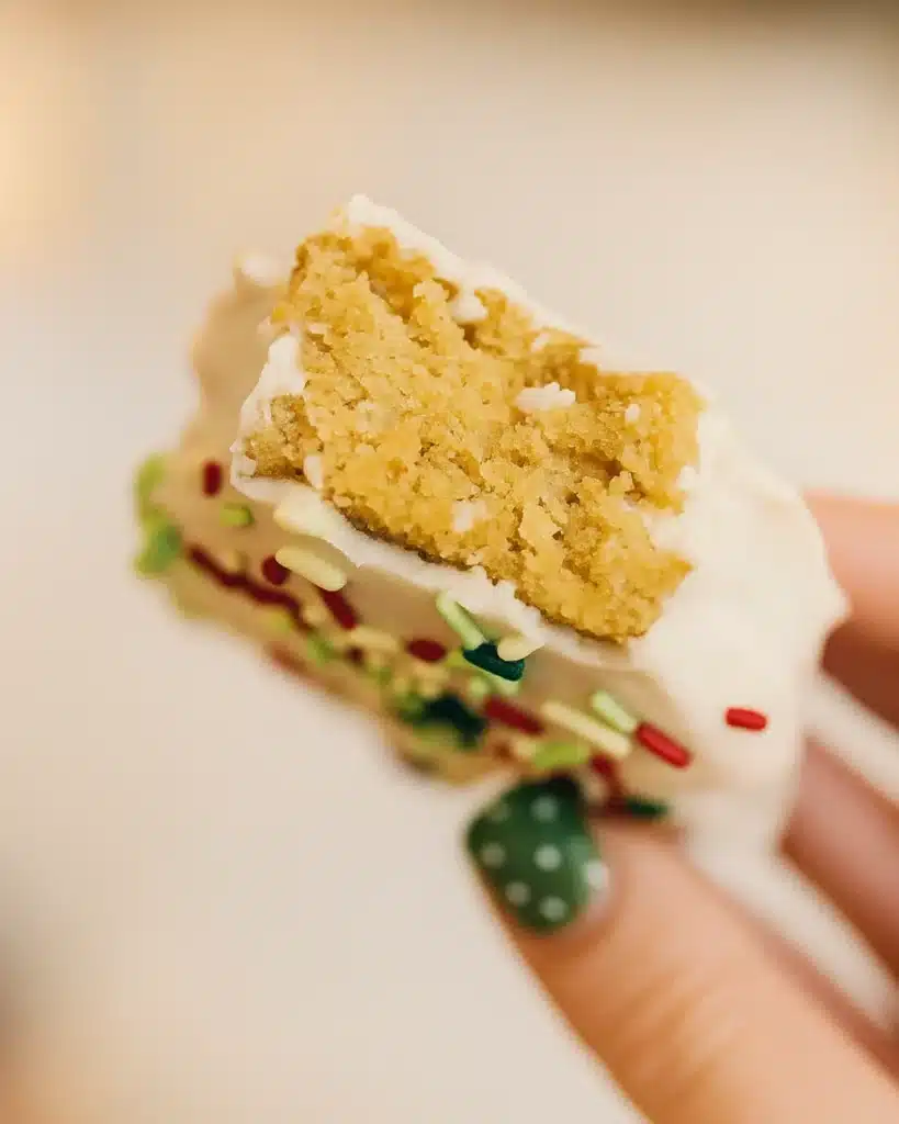 Hand holding a bitten Christmas tree cake with white icing and sprinkles