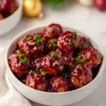Festive cranberry meatballs in white bowl with glossy cranberry sauce and parsley