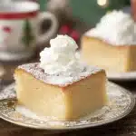 Eggnog magic cake slice with whipped cream and powdered sugar on festive plate