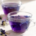 Purple butterfly pea tea in glass cups on a marble surface with dried flowers