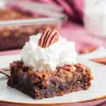 Slice of pecan pie brownie topped with whipped cream and pecan half