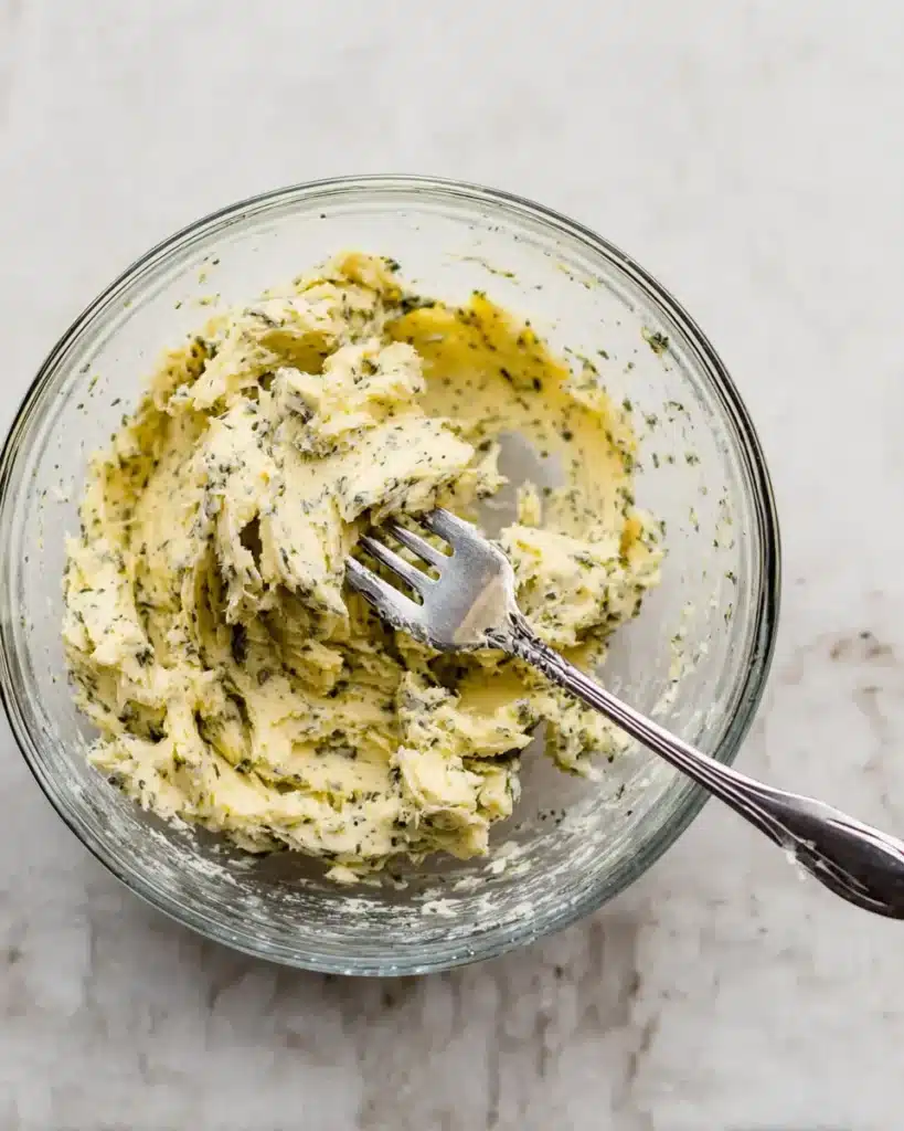 Garlic herb butter mixture in glass bowl with fork on marble surface
