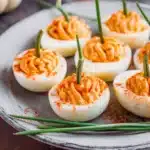 Pumpkin patch deviled eggs with paprika and chive stems on a gray plate