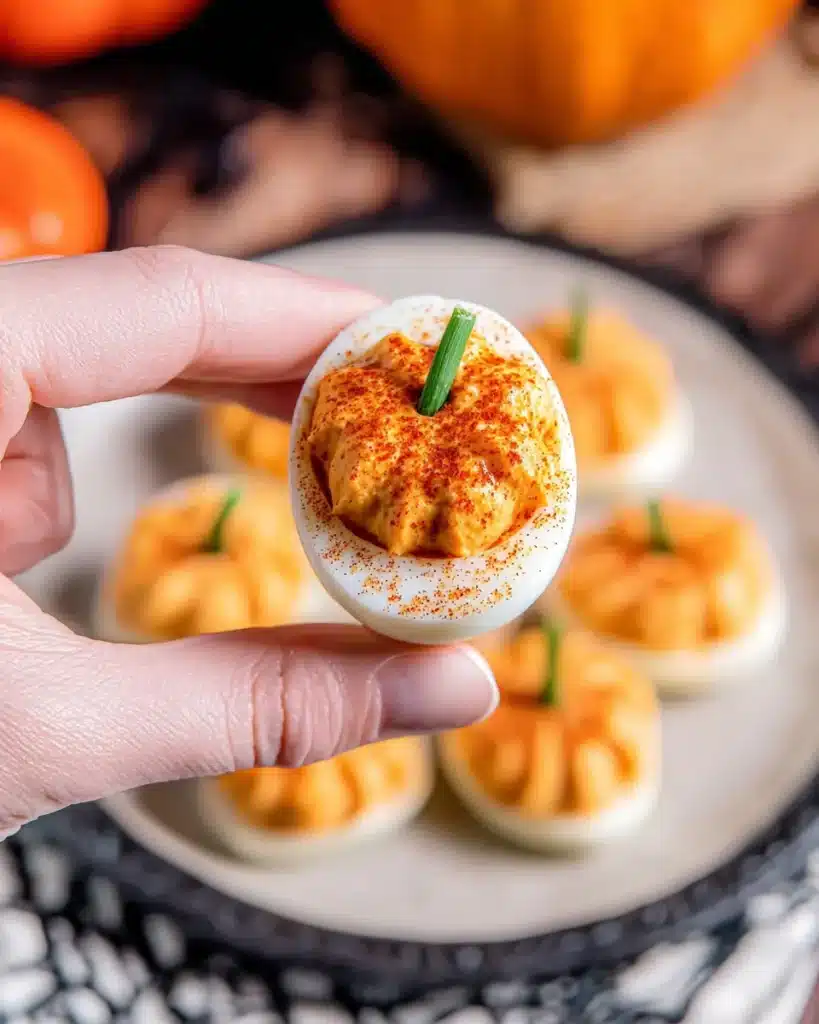 Hand holding Pumpkin Patch Deviled Egg with paprika and chive stem