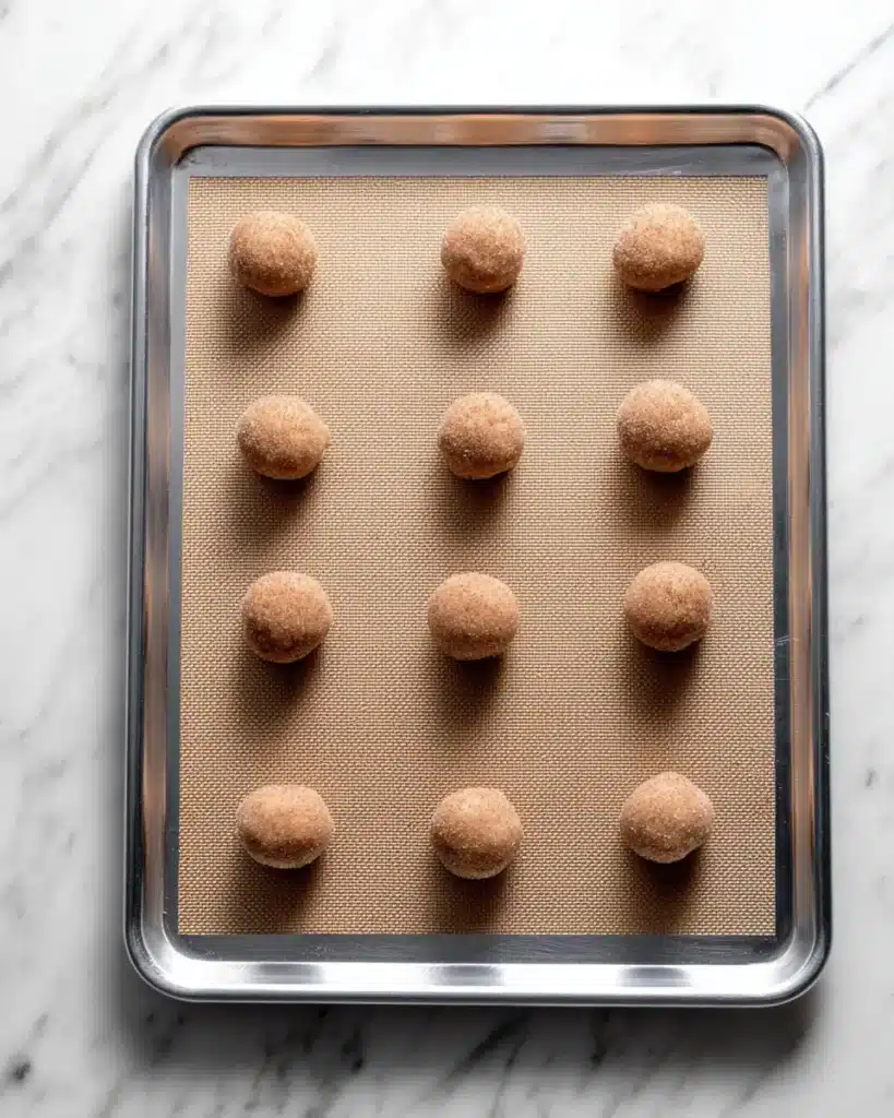 Snickerdoodle cookie dough balls arranged on a silicone baking mat, coated in cinnamon sugar.