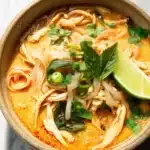 Thai chicken curry soup with noodles, chicken, herbs, and lime in a creamy coconut broth