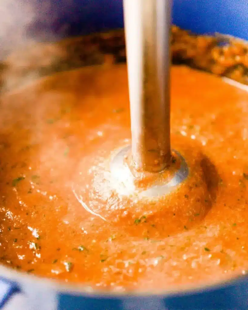 Blending tomato basil soup with immersion blender in a blue pot