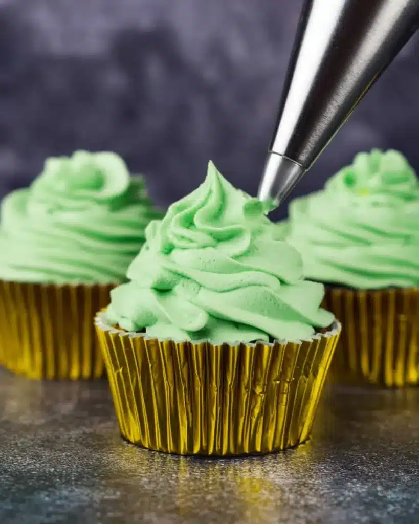 Piping green frosting onto cupcakes with gold liners